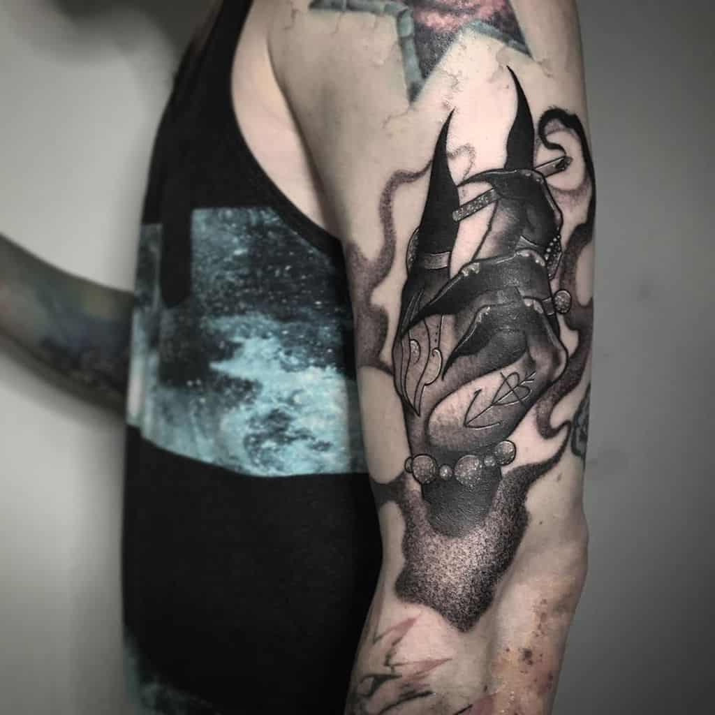 Dark black and grey tattoo of a sinister hand with long claws, holding mystical beads, surrounded by eerie smoke on the upper arm.