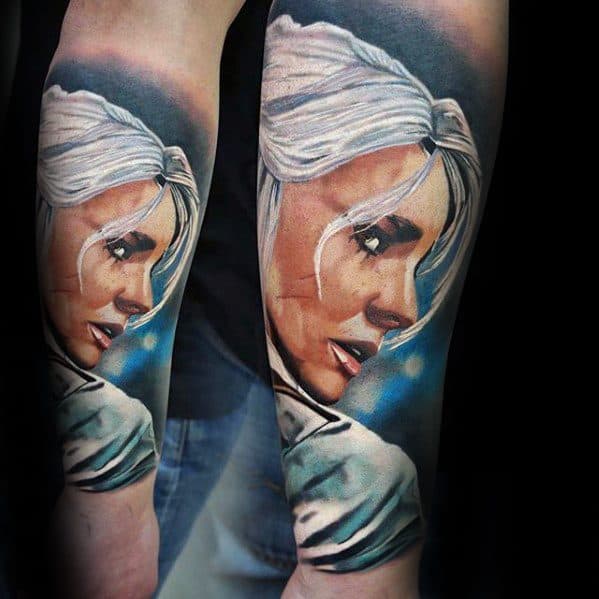 Vibrant color tattoo of Ciri from The Witcher on the forearm, showing her white hair, scar, and a soft blue glowing background.
