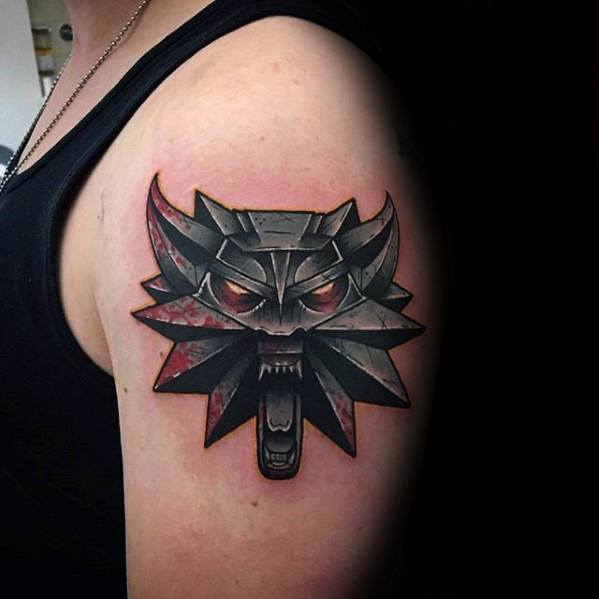 Bold upper arm Witcher tattoo of the wolf medallion with sharp edges, glowing red eyes, and a splash of red behind for added impact.