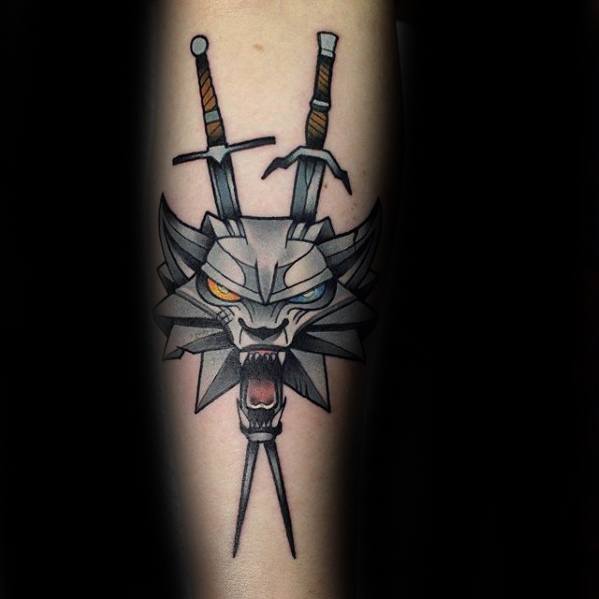 Bold Witcher tattoo on the forearm featuring the snarling wolf medallion with yellow and blue eyes, and two crossed swords above.