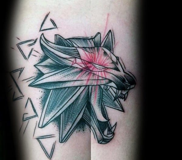 Sketch-style Witcher tattoo of the wolf medallion with bold shading, red claw marks across the eye, and dynamic angular fragments.