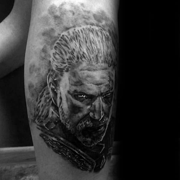Realistic black and grey tattoo of Geralt from The Witcher with intense expression, scarred face, and detailed armor on the upper arm.