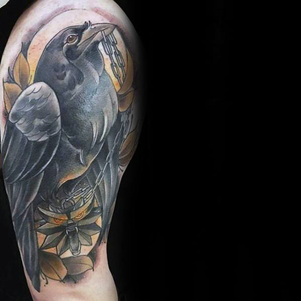 Witcher-inspired upper arm tattoo featuring a black raven perched above a wolf medallion, with warm golden tones and stylized leaves.