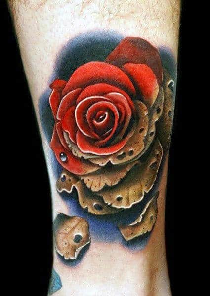 Realistic tattoo of a red rose with aged, decaying petals on a dark, shadowy background, placed on the lower leg