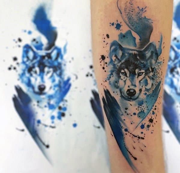 Forearm wolf tattoo with dynamic blue watercolor splashes, ink splatters, and a sharp gaze, mirrored by matching stencil art in the background.