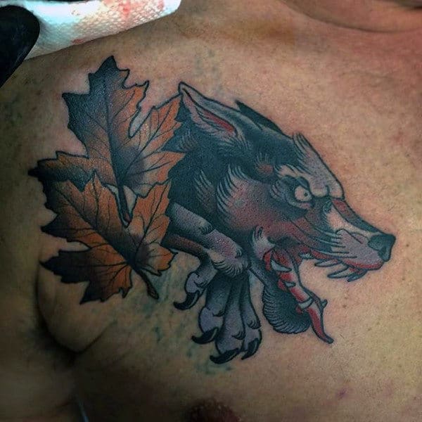 Tattoo of a snarling Japanese wolf head with red eyes and tongue, beside two autumn leaves on a chest