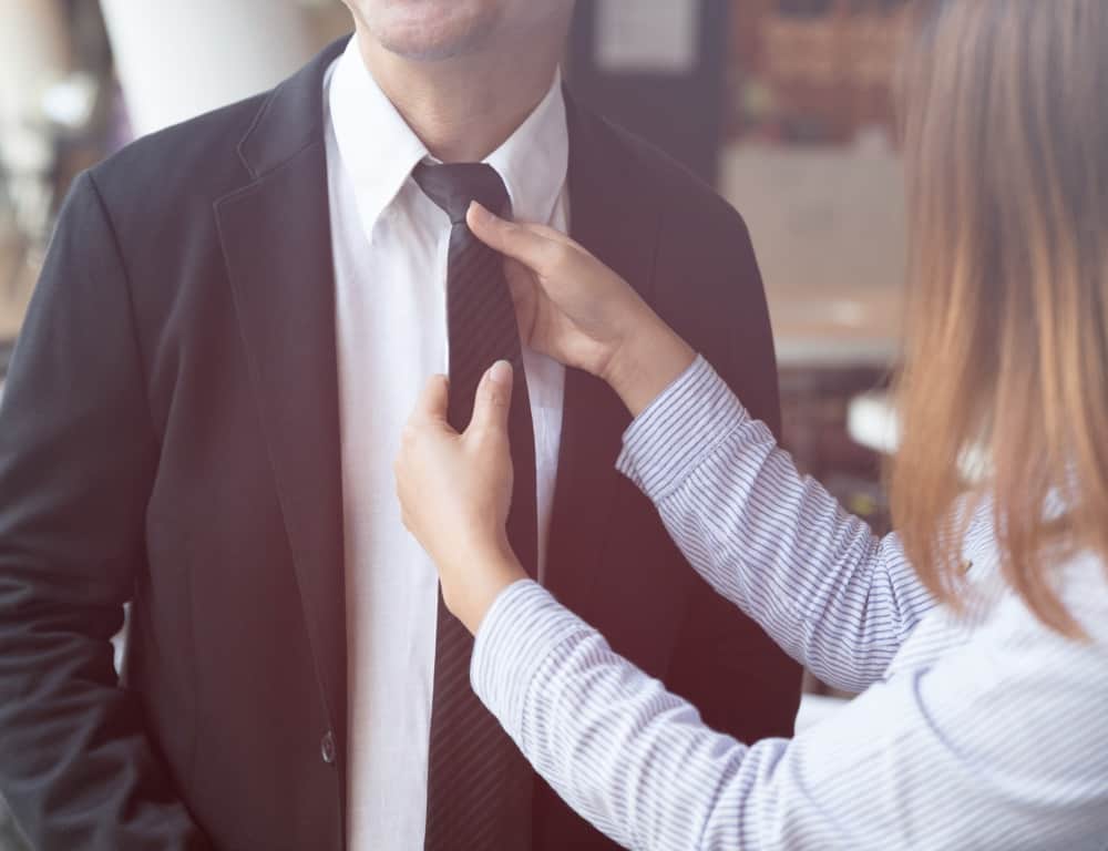 woman adjusting the black tie of a man suit
