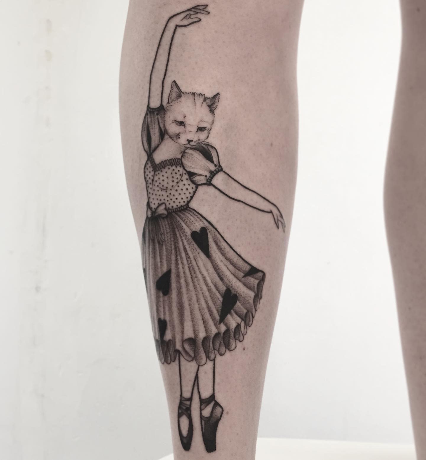 Elegant black and grey tattoo of a ballerina with a cat’s face, wearing a vintage dress with heart patterns
