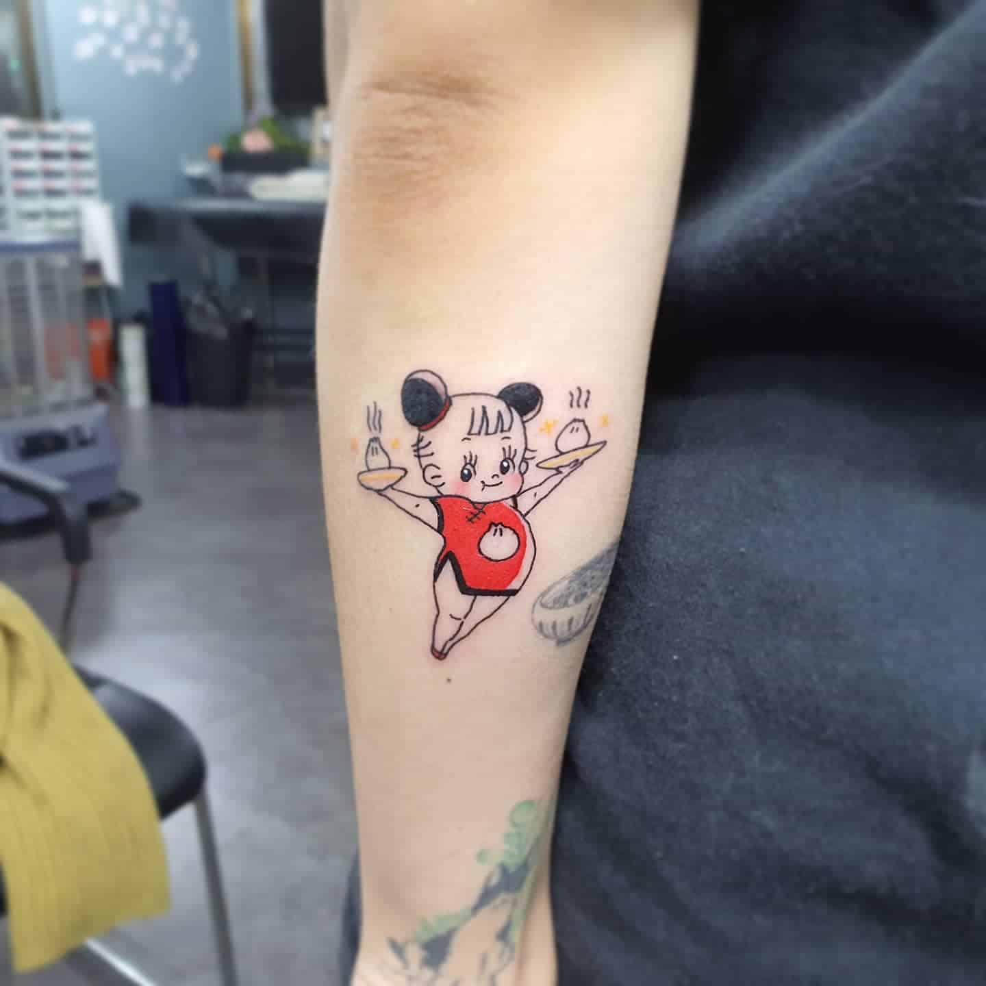 Adorable tattoo of a dumpling-themed girl in a red outfit, balancing steaming buns