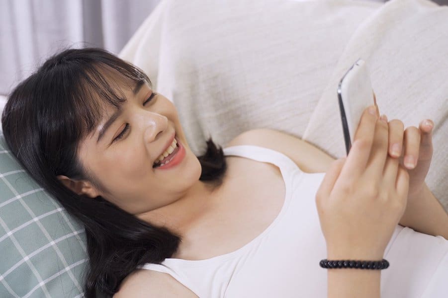 woman lying in sofa bed reading funny texts from her boyfriend