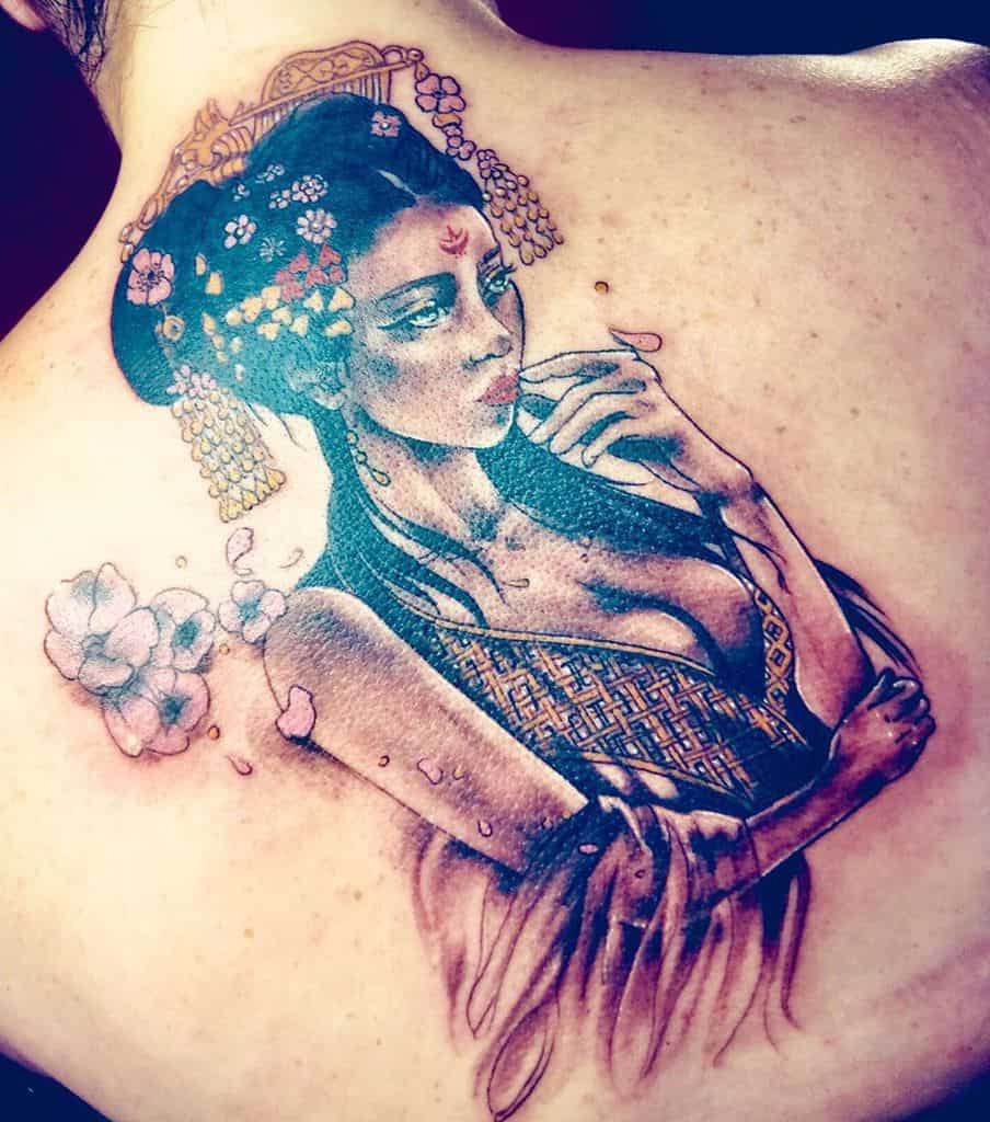 Elegant back tattoo of a Geisha with intricate golden hair ornaments, flowing garments, and delicate cherry blossoms in a blend of realism and fantasy.