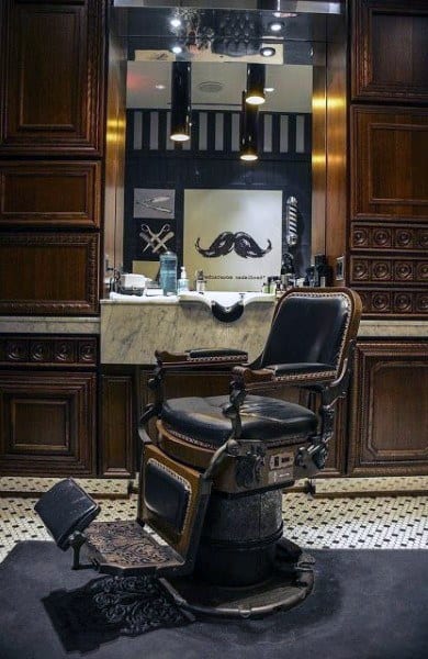 Vintage barber chair with leather upholstery, wooden panel walls, and marble countertop.