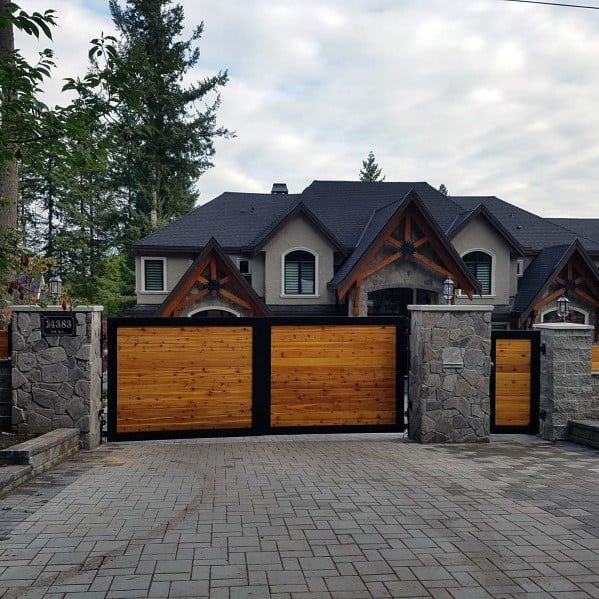 Wooden driveway gate with black metal frame and stone pillar accents.