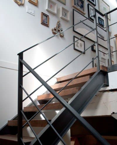 Modern wooden staircase with sleek metal railing and framed art on the crisp white wall