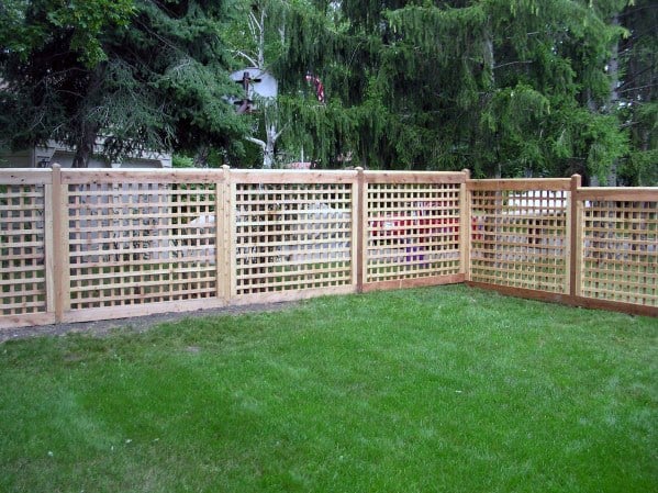 Wood lattice fence encircles a lush green lawn, framed by towering trees