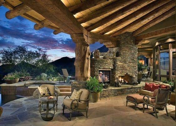 Elegant pavilion with large log beams, stone fireplace, cozy seating, and a stunning mountain view at sunset.