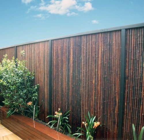 Metal-framed bamboo fence with rich dark bamboo panels behind a raised planter box in a modern rooftop garden.