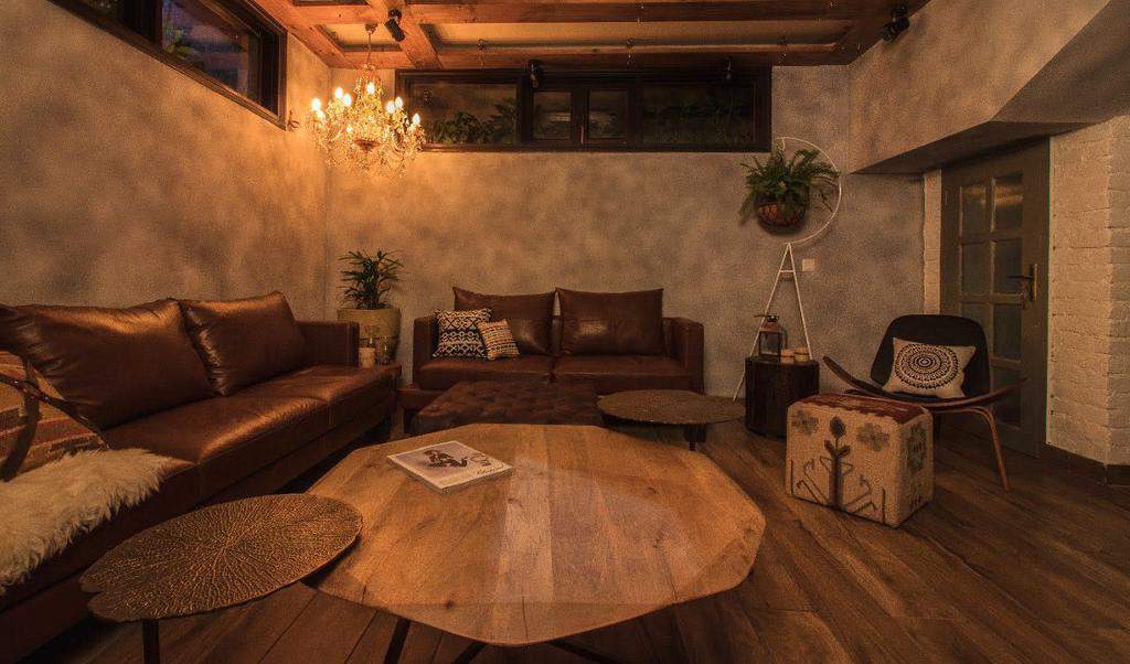 Dark modern living room with brown leather couches, wooden coffee table, and chandelier.