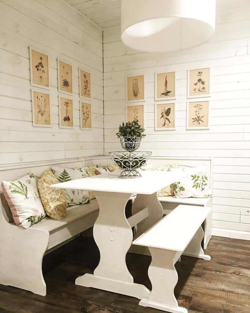 White wood-paneled nook with a farmhouse-style table, bench seating, and botanical wall art.