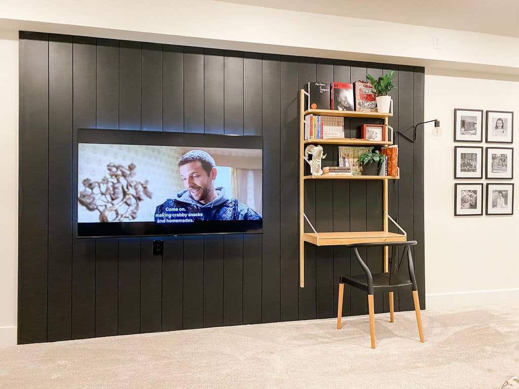 Basement living room with black accent wall, wall-mounted TV, and small wooden desk setup.