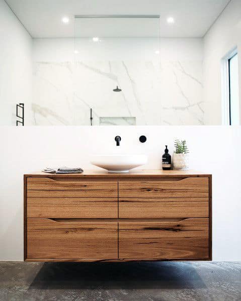 Minimalist floating wood vanity with vessel sink and marble accent wall.