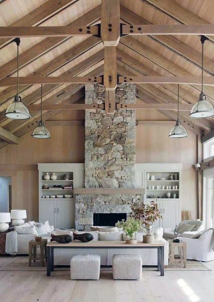 Rustic living room with exposed wood beam ceiling, stone fireplace, white sofas, and pendant lights.
