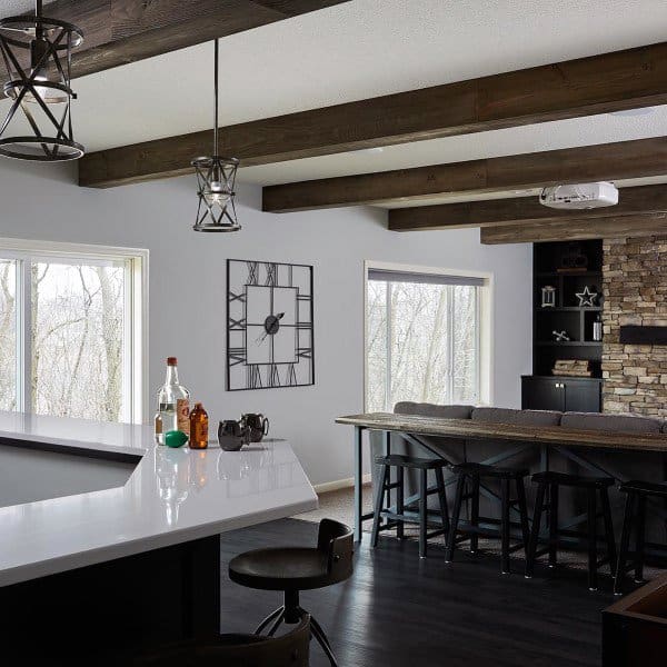 Modern basement bar with exposed wooden beams, stone accent wall, and large windows.