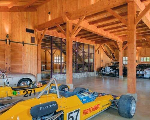 Wooden garage with exposed beams, race cars, vintage vehicles, and barn-style architecture.
