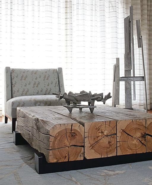 A modern living room with a rustic wooden coffee table, a patterned armchair, and abstract metal sculpture