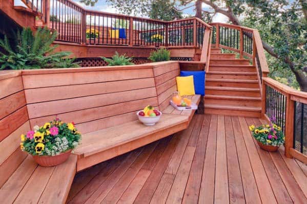 Wooden deck with a cozy bench, potted flowers, fruit bowl, and stairs leading to an upper level