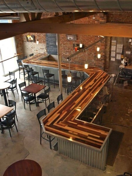 L-shaped wooden bar top with mixed wood tones, industrial metal siding, and exposed brick walls.