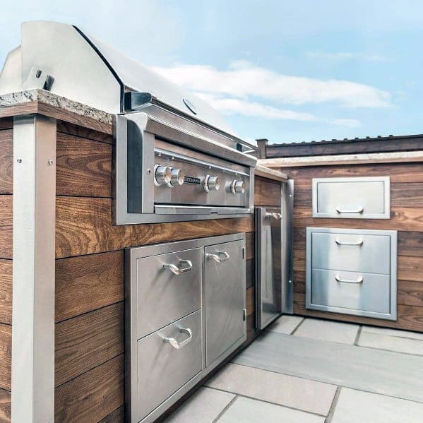 Modern outdoor kitchen with a built-in stainless steel grill and wooden cabinets under a blue sky
