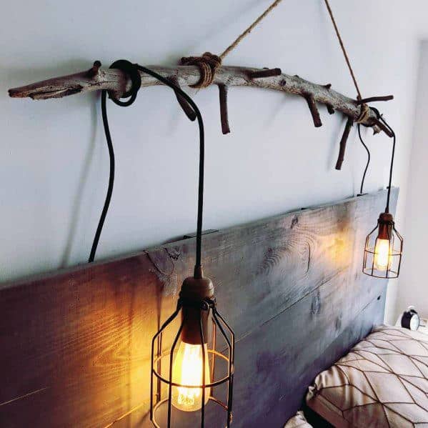 Rustic bedroom with branch hanging industrial pendant lights over wood headboard.
