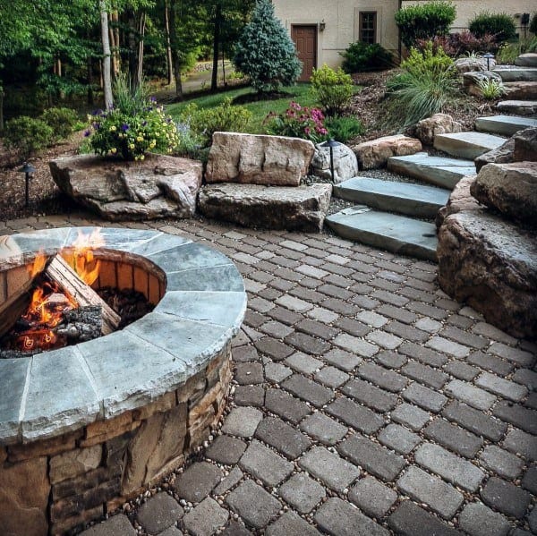 Backyard patio with a cozy fire pit, surrounded by greenery and steps leading to a house
