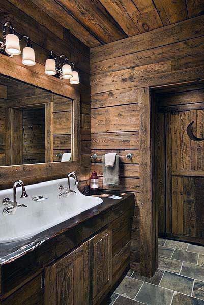 Rustic half bath with wooden walls, large mirror, double sink, and overhead lights featuring a moon design on the wooden door