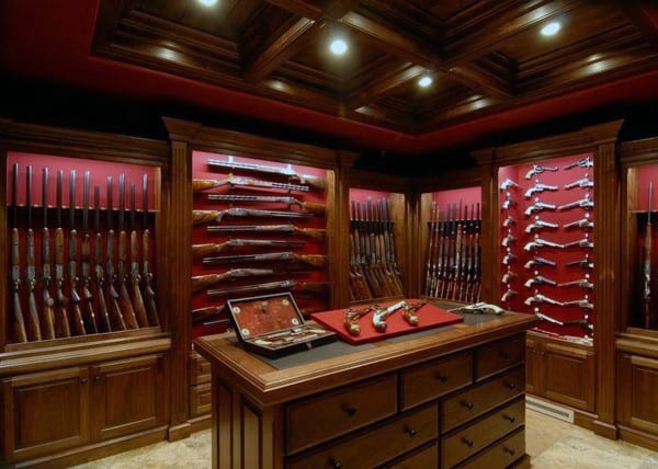 Luxury gun room with wooden cabinets, red velvet backing, and a central display table.