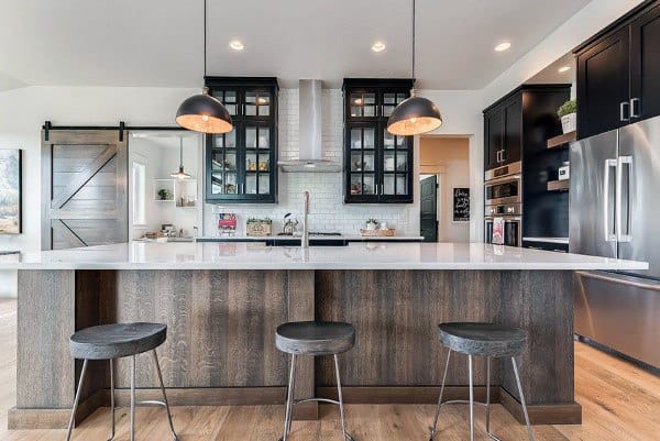 Modern rustic kitchen with a dark wood island, black cabinets, barn door, and pendant lighting.