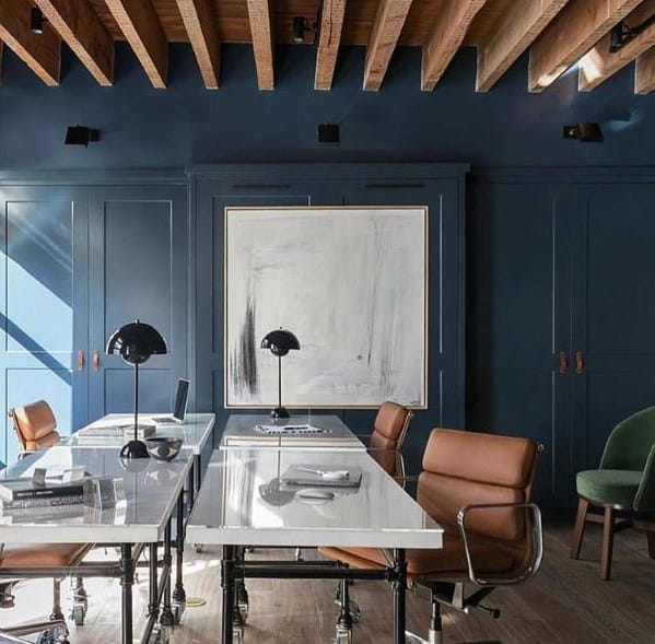 Modern office with exposed wood beam ceiling, navy walls, white desks, and leather chairs.