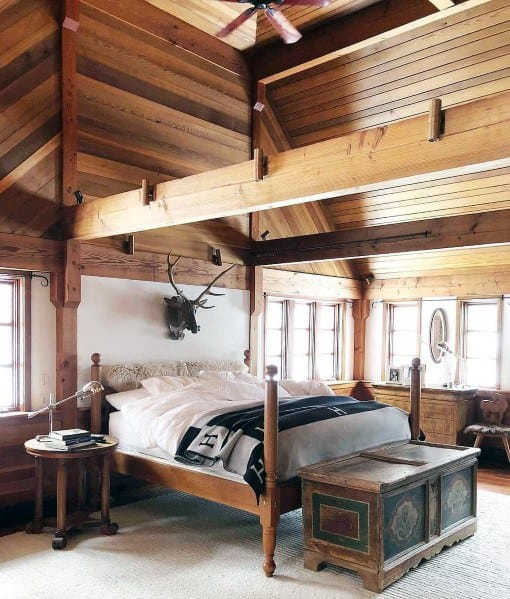 Rustic bedroom with exposed wood beam ceiling, wooden walls, four-poster bed, and vintage decor.