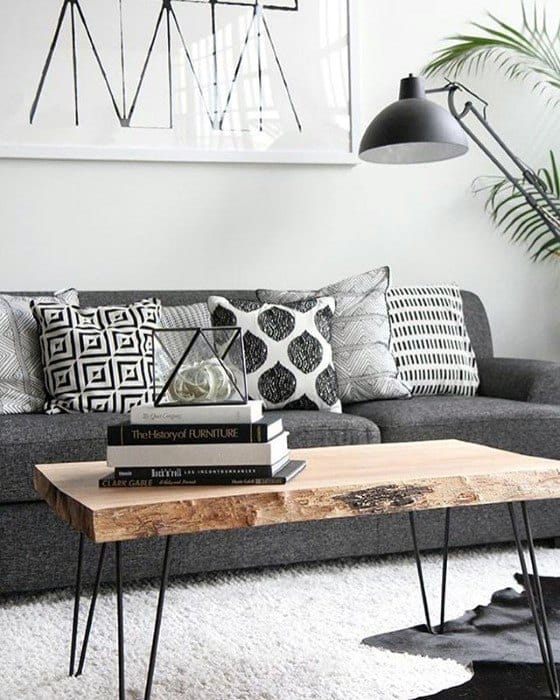 Natural wood slab coffee table with metal legs in a modern living room with a grey sofa and geometric pillows.