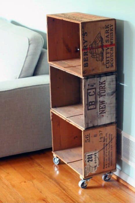 Wooden crates repurposed as a shelf, stacked vertically with caster wheels, next to a sofa