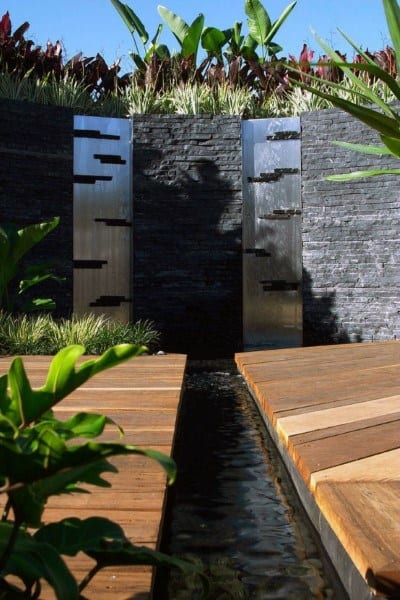 Modern backyard waterfall with sleek metal accents, wood decking, and lush tropical plants.