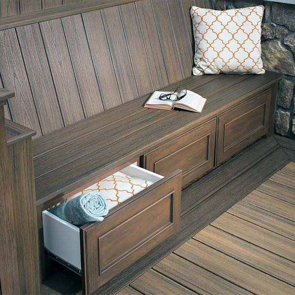 A wooden bench with an open drawer reveals a towel and pillow; atop, a book and glasses rest beside another pillow