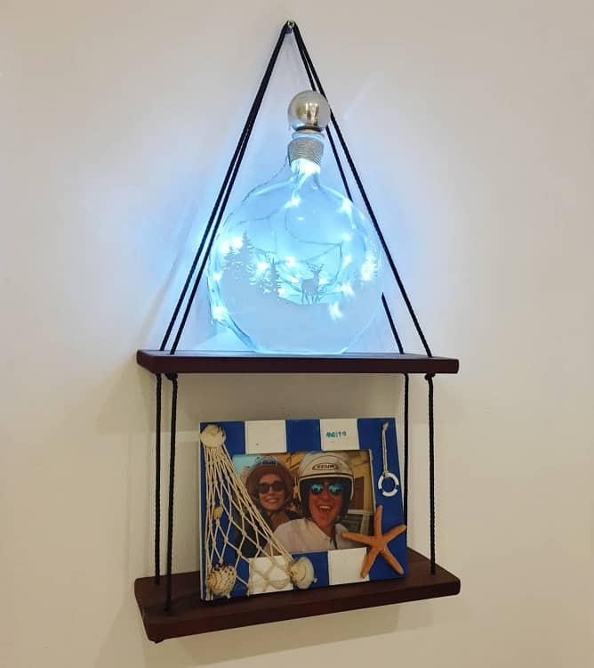 Hanging wooden bathroom shelf with decorative light bottle and framed photo.