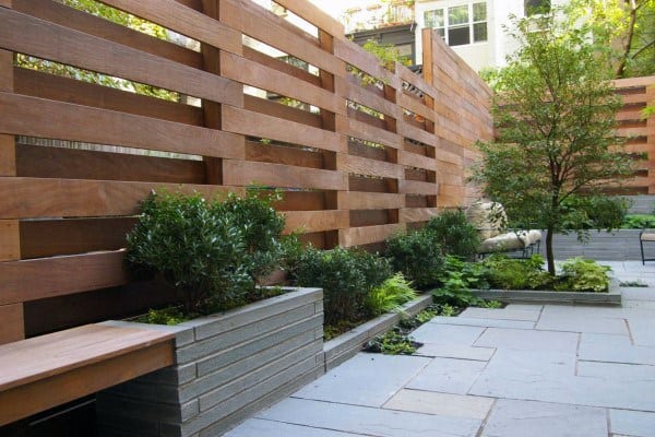 Contemporary wooden screen fence with elevated planters and vibrant greenery in a backyard patio.