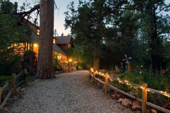 Charming gravel driveway lined with warm rope lights along a wooden fence, creating a cozy and inviting atmosphere leading to the home