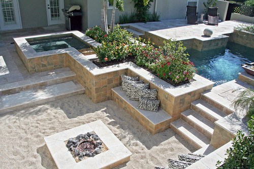 Luxurious backyard with a pool, hot tub, fire pit area, stone seating, and lush greenery