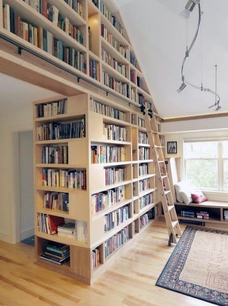 A cozy home library with tall bookshelves, a ladder, and a reading nook by the window