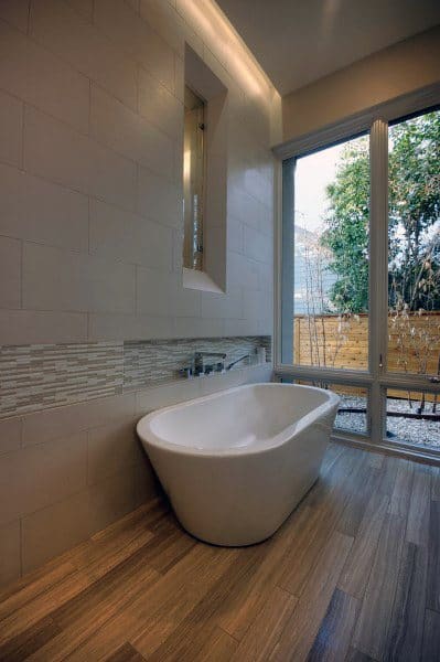 Modern bathroom with white bathtub, large window, and wooden floor tiles