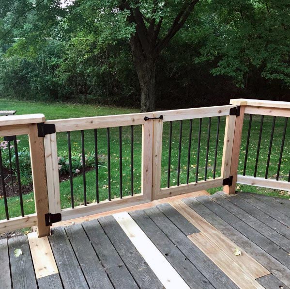 Wooden deck with railing and gate overlooking a green lawn and trees